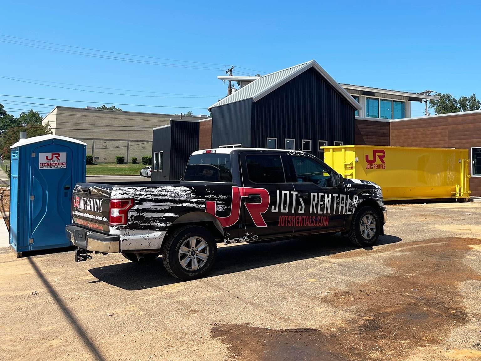 A JOTS Rentals truck with a portable restroom and roll-off dumpster