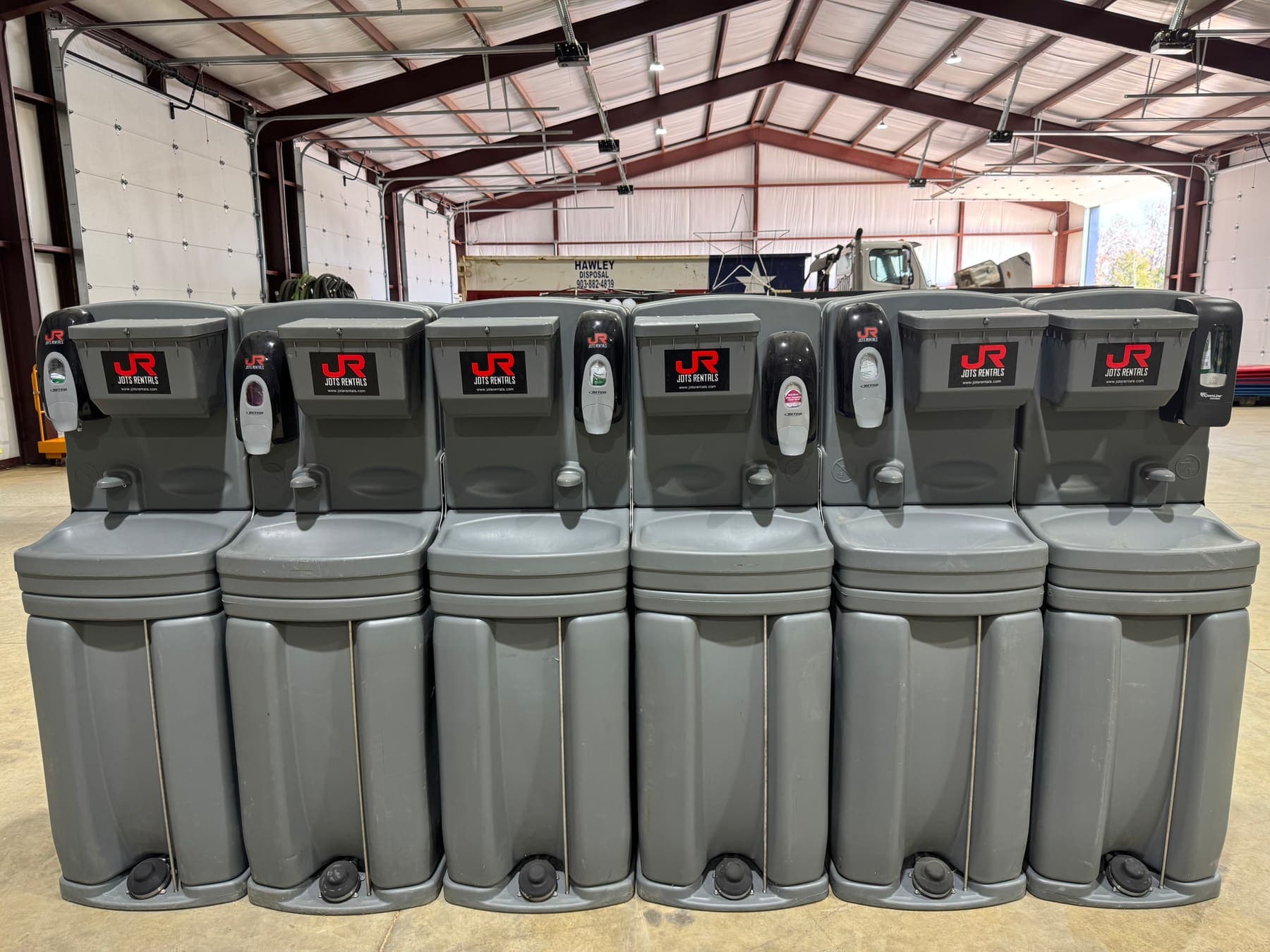A row of grey JOTS Rentals foot-pump hand-wash stations ready for delivery